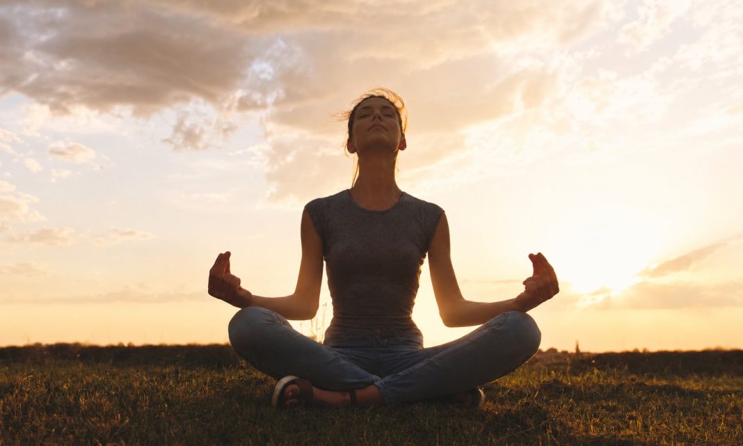 Woman seated quietly in a grassy field at sunset