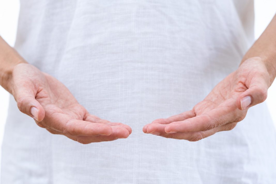 Close-up of empty open hands in front of a white garment.