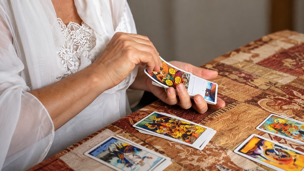 Hands in a white blouse arranging tarot cards on a home table.