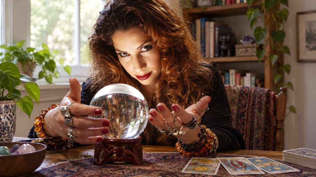 Home reader portrait repaired Woman with curly brown hair at a modest home table with cards and a small clear glass ball.