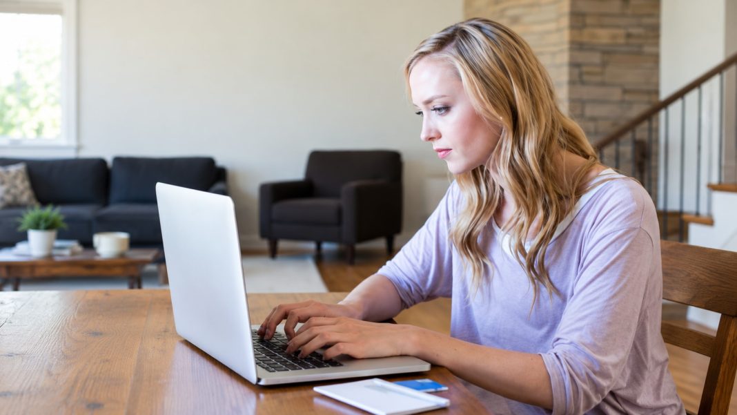 Review browsing photograph repaired Blonde woman in a lavender top typing on an ordinary laptop at a wooden table.